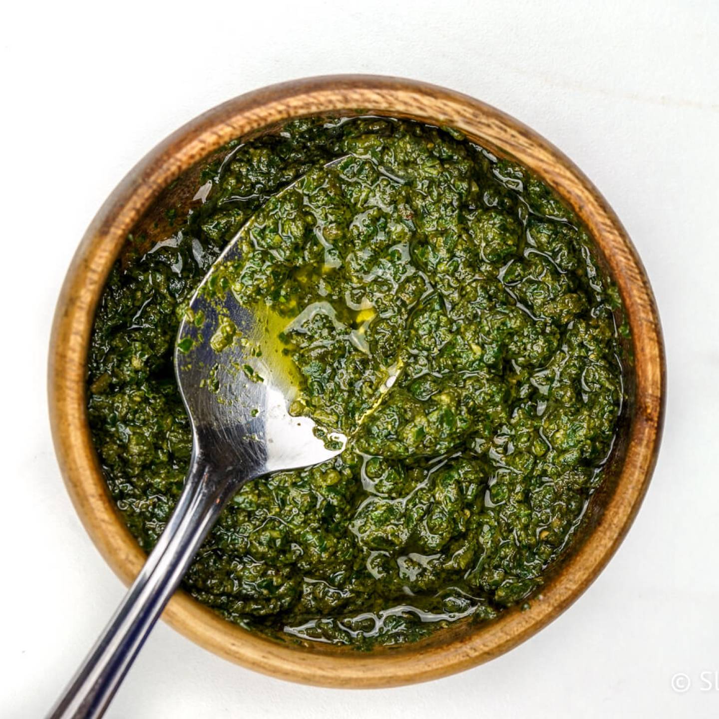 Skinny pesto in a wooden bowl with olive oil and a spoon.