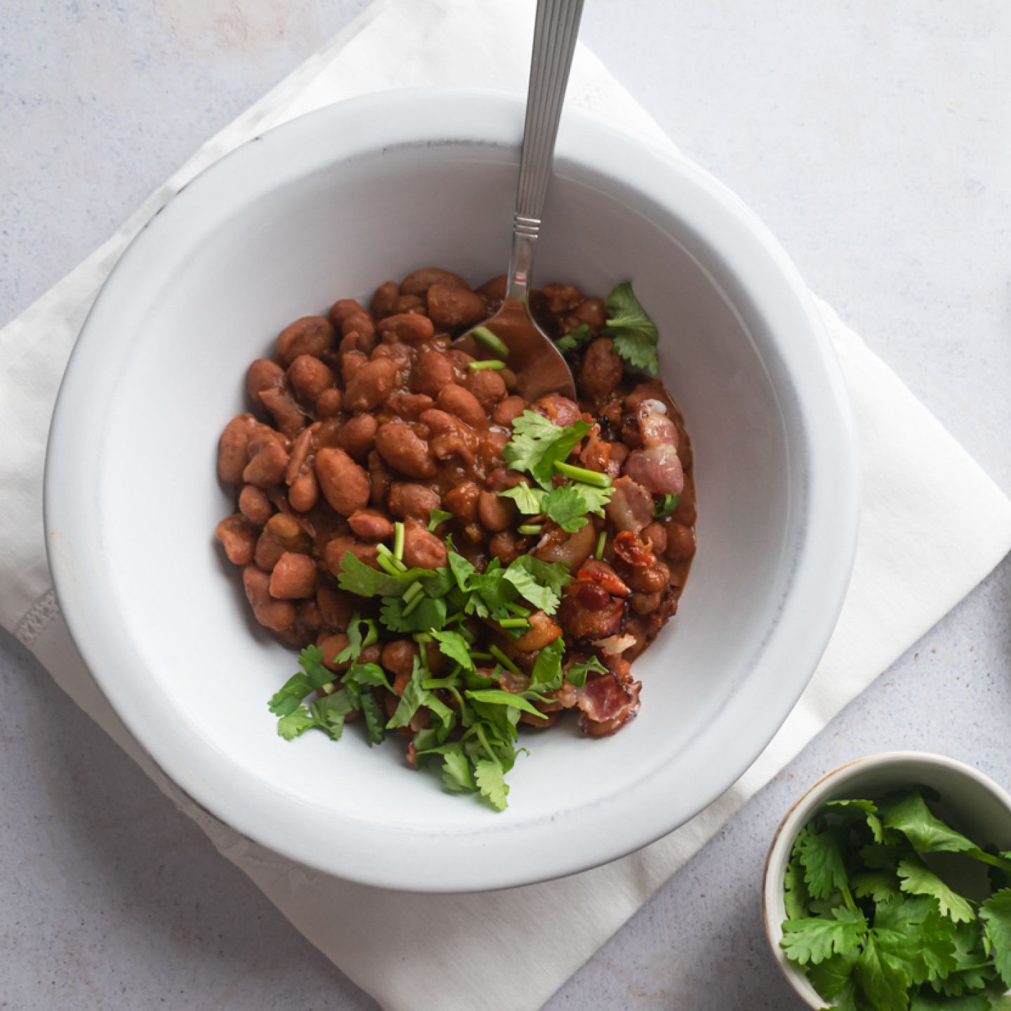 Slow cooker borracho beans in a bowl with cilantro, crispy bacon, and beer broth.