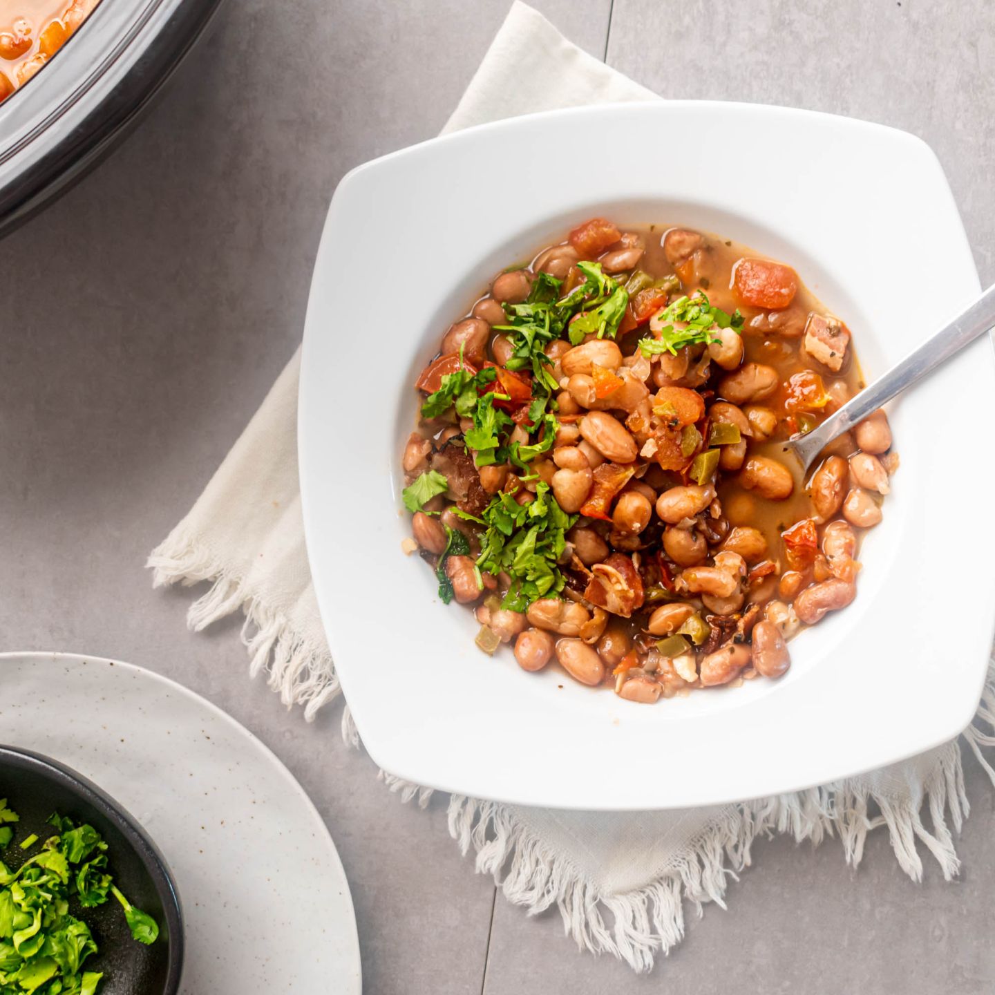 Slow cooker frijoles charros, cowboy beans, in a bowl with creamy pinto beans, jalapenoes, tomatoes, onions, and fresh cilantro.