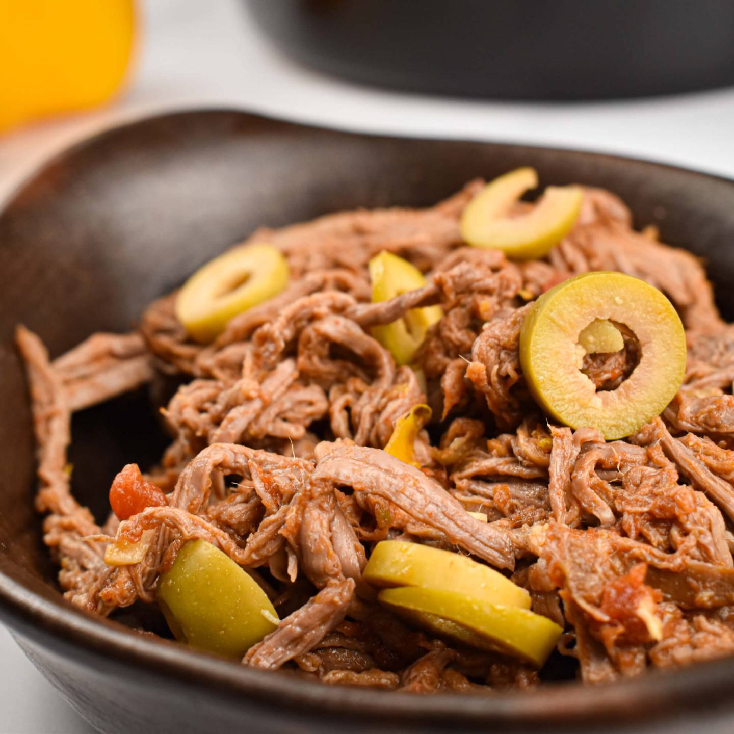 Slow cooker ropa vieja with peppers, onions, tomatoes, and olives in a black dish.