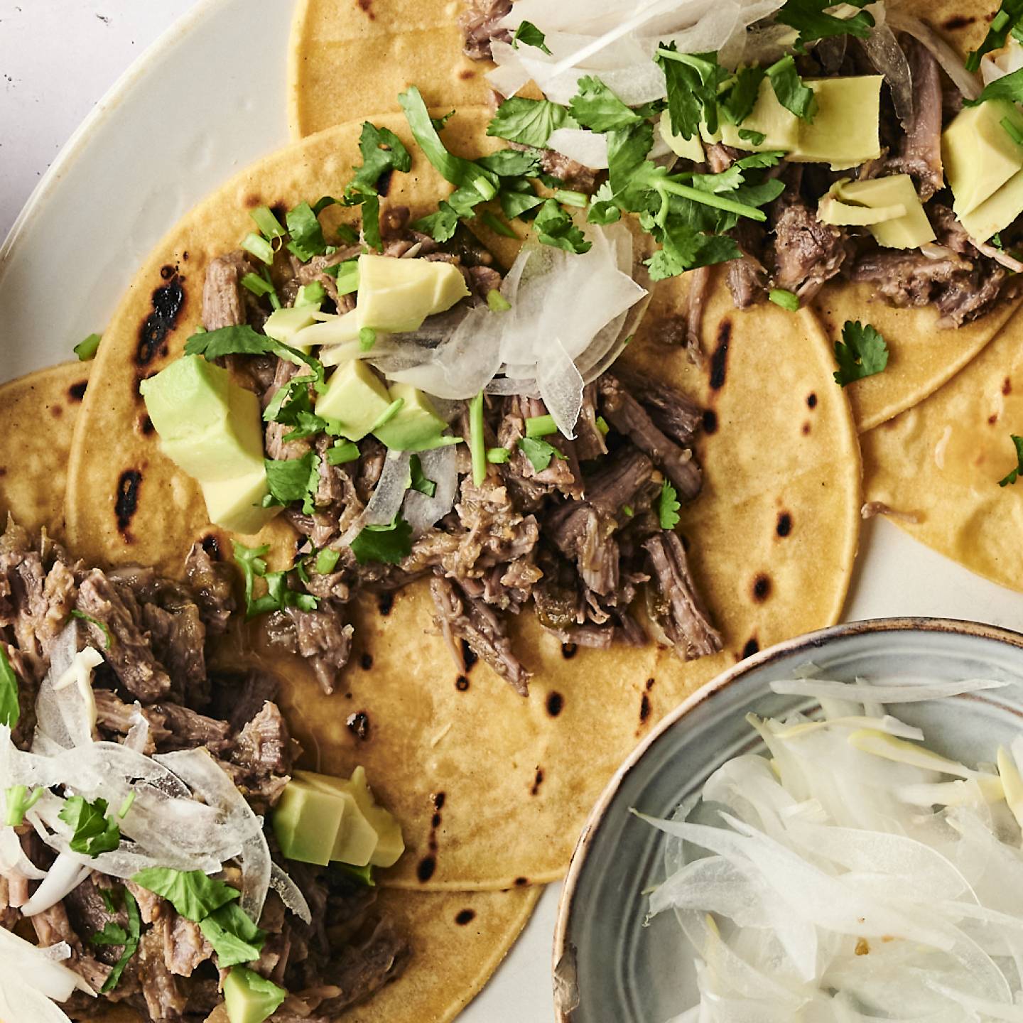 Shredded salsa verde beef served in corn tortillas, garnished with chopped onions, sauce, and fresh cilantro.