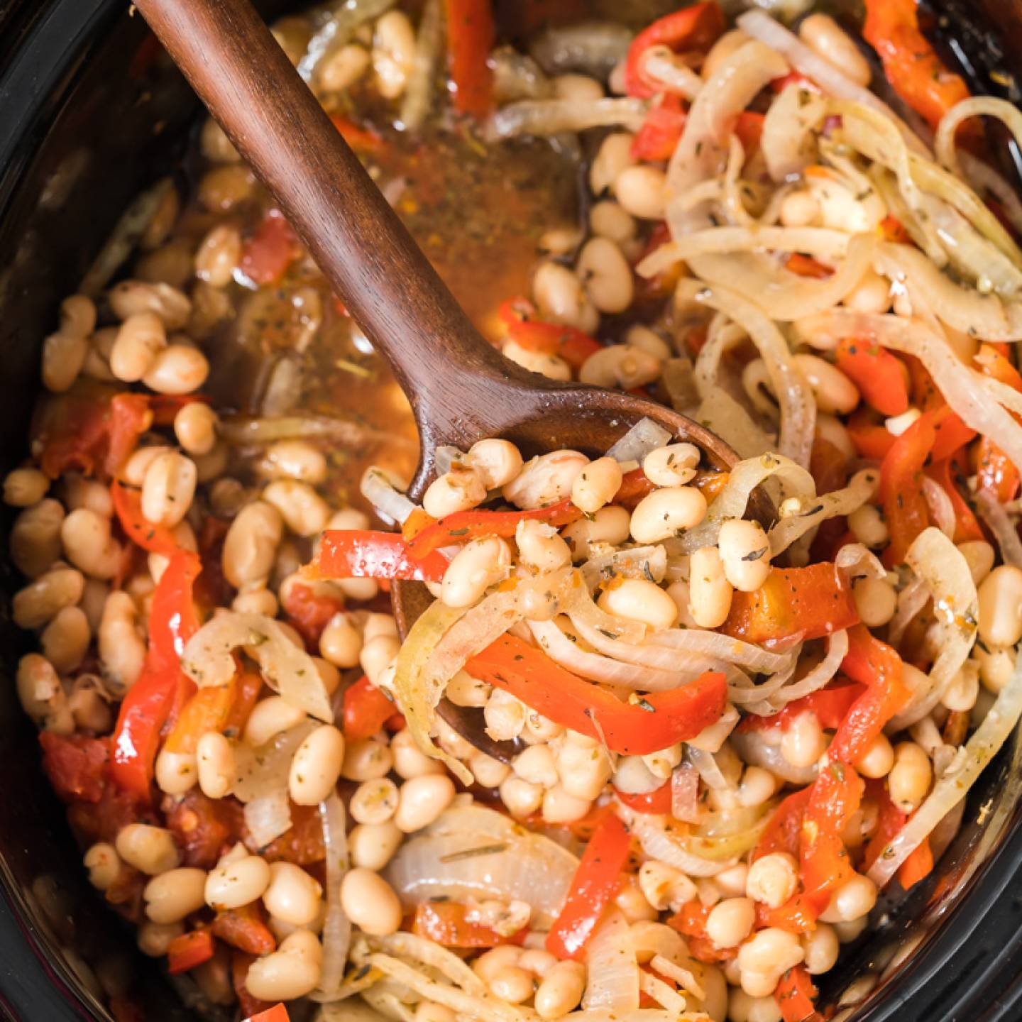 Slow Cooker Tuscan white beams with sliced red peppers, sliced onions, white beans, and spices in the crockpot.