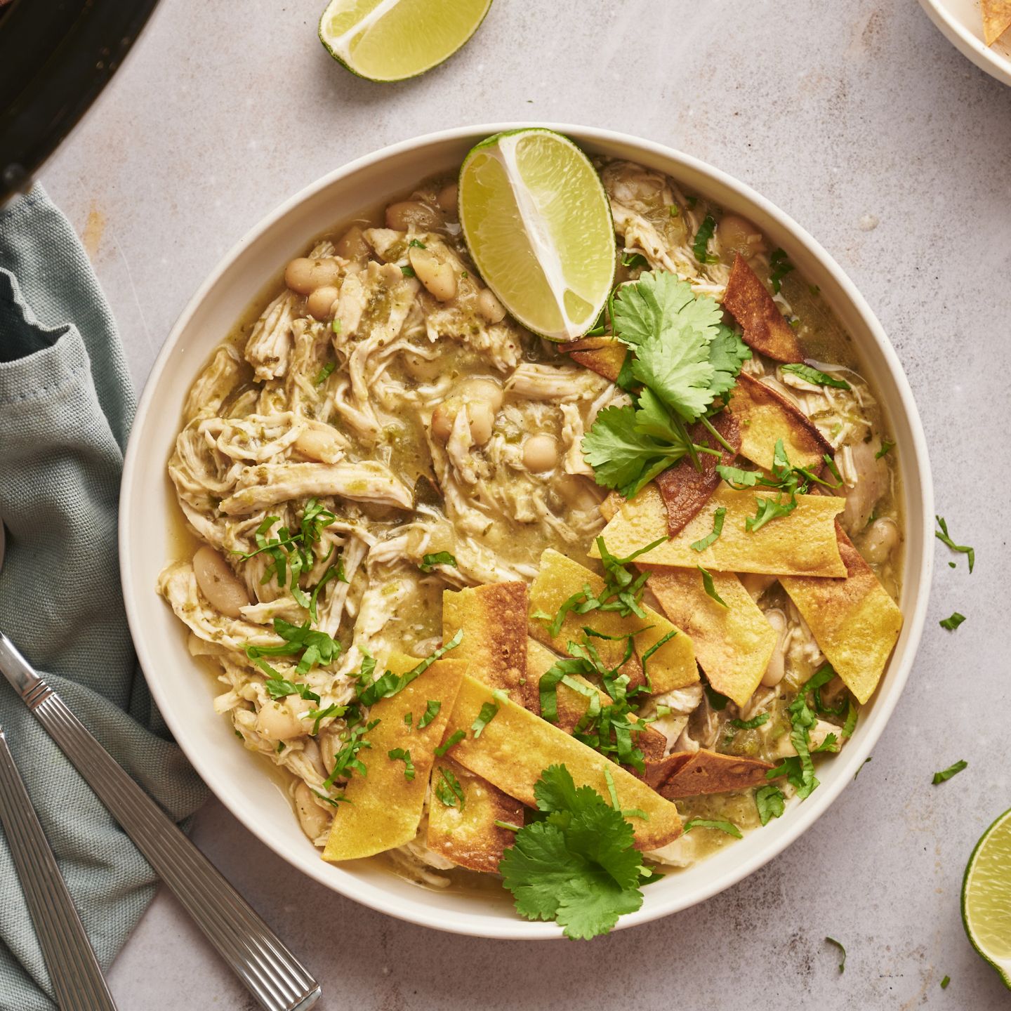 Slow cooker white chicken chili with shredded chicken, green chilies, white beans, tortilla chips, cilantro, and lime.