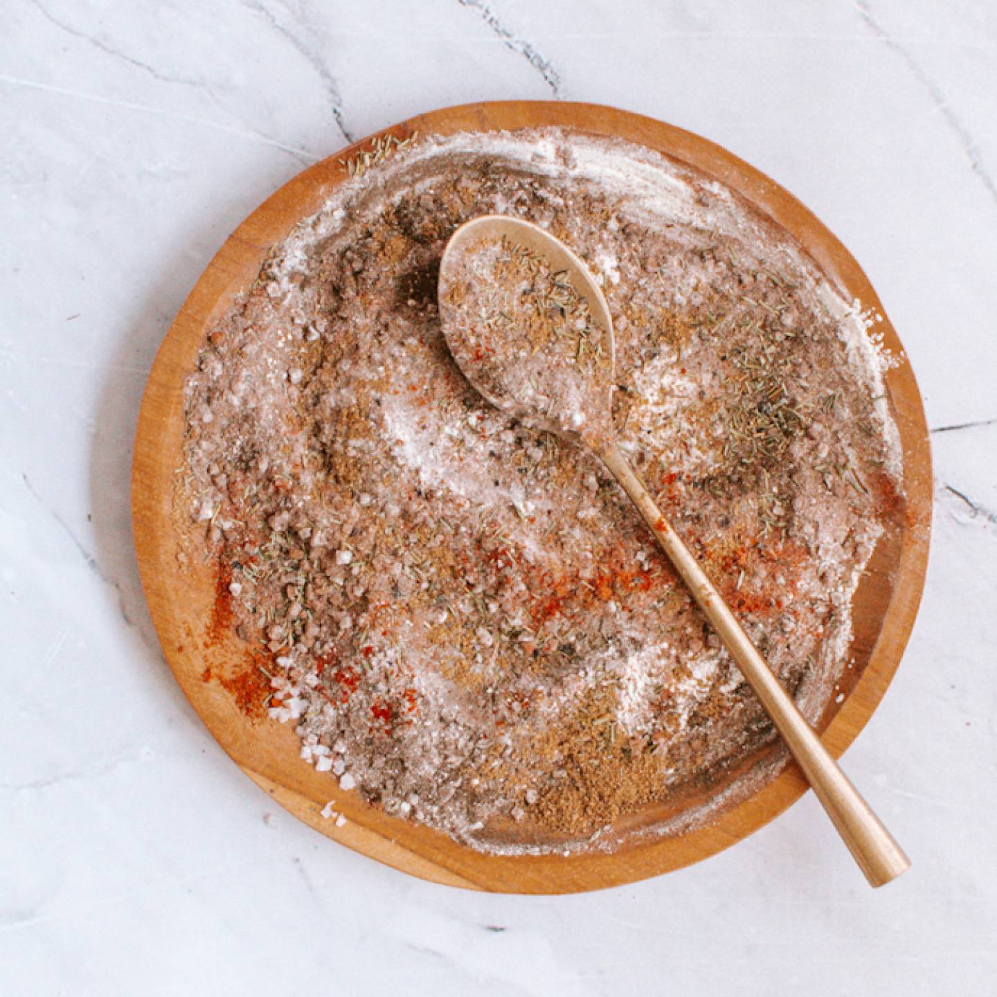 Steak seasoning with kosher salt, pepper, paprika, garlic powder, onion powder, and herbs on a wooden plate.