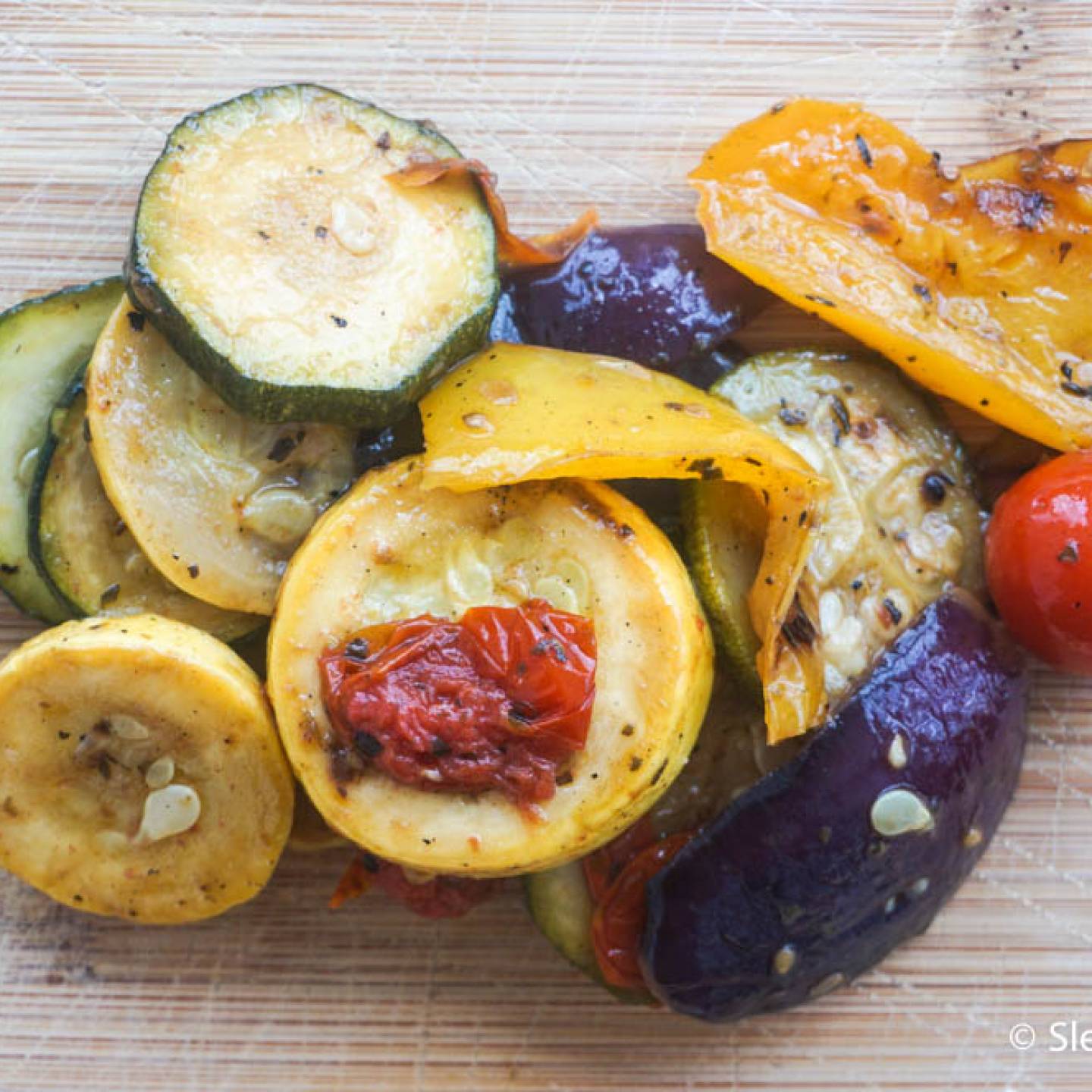 Grilled summer vegetables with zucchini, yellow squash, cherry tomatoes, red onion, and red bell peppers on a cutting board.