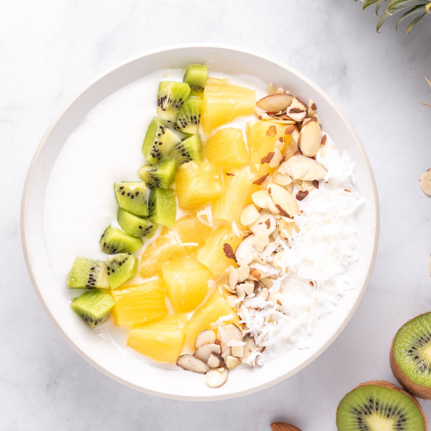 Tropical yogurt bowl with sliced pineapple, kiwi, almonds, and shredded coconut layered in a bowl.