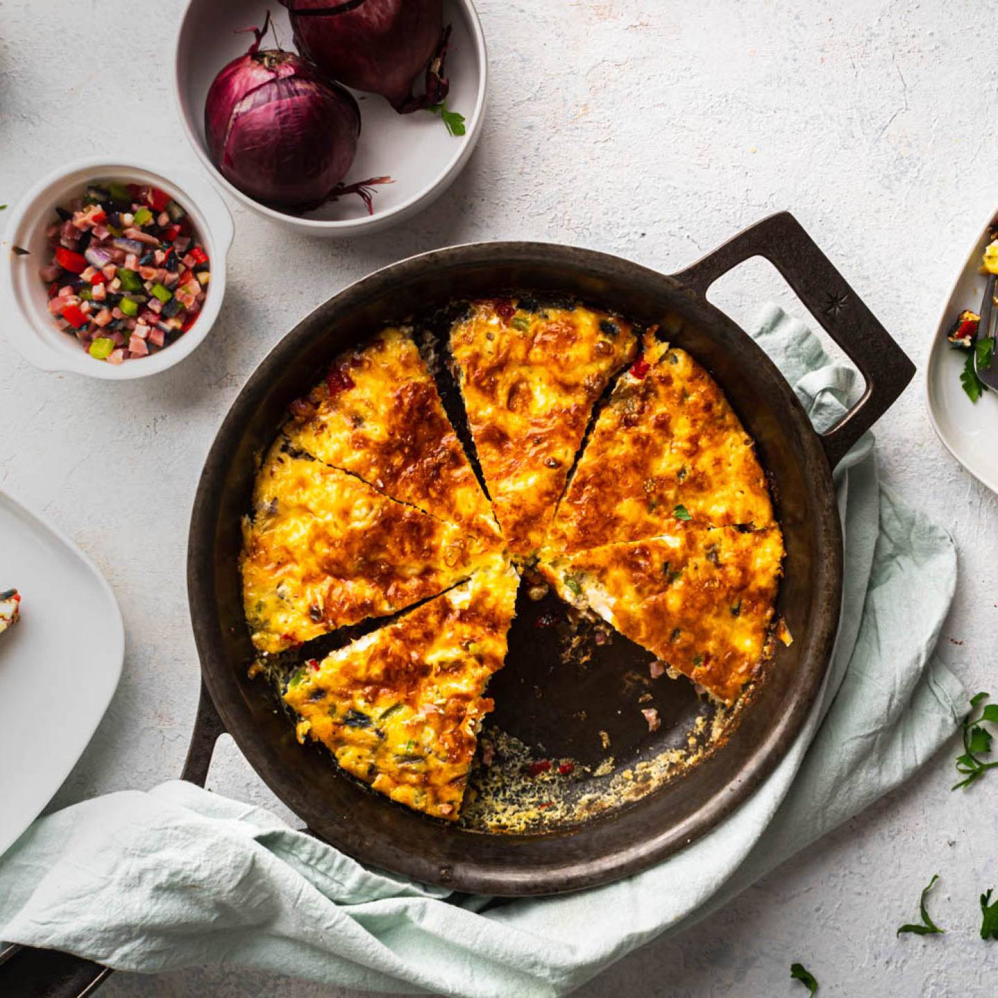 Western omelet frittata with peppers, onions, ham, and cheese cooked in a cast iron skillet and served with fresh parsley.