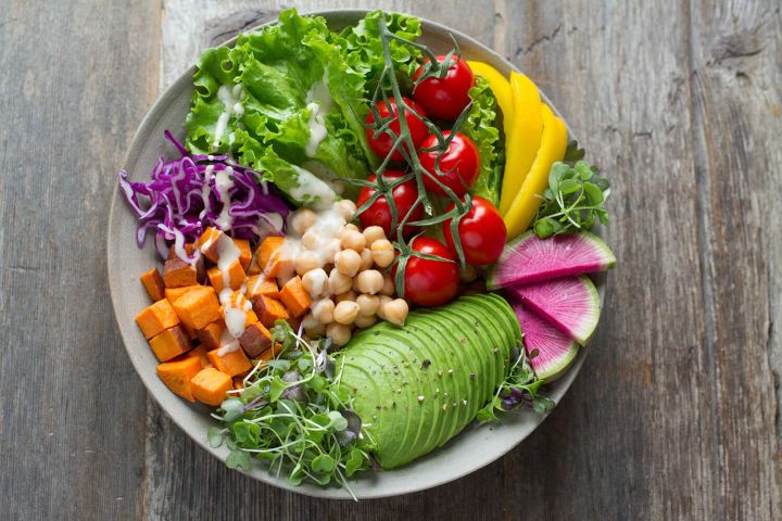 Clean eating dish with avocado, tomatoes, peppers, cabbage, carrots, and chickpeas.