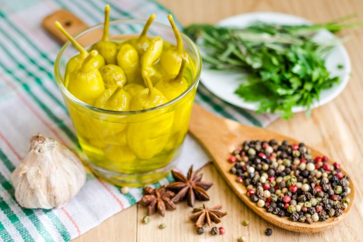 Pepperoncinis in a glass dish with peppercorns, garlic, and herbs.