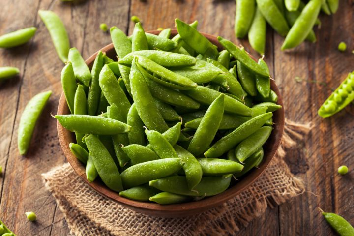 Raw sugar snap peas ion a bowl on a wooden countertop.