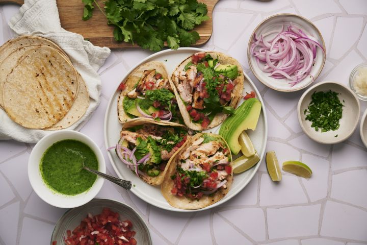 Mexican chicken tacos with tomatoes, onions, tortillas, salsa, and cilantro.