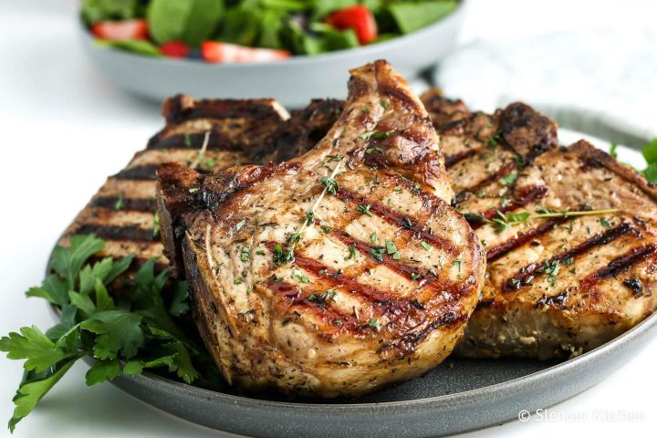 Healthy grilled pork chops on a plate with fresh herbs and salad.