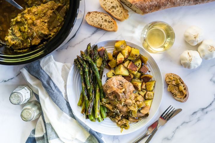 Forty clove of garlic chicken breasts cooked with whole garlic cloves and leeks on a plate with roasted potatoes and asparagus.