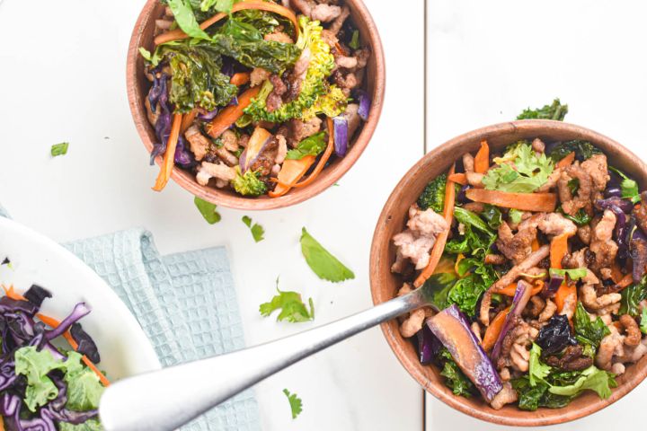 Asian ground turkey stir fry with kale, carrots, broccoli, and soy sauce in two bowls.