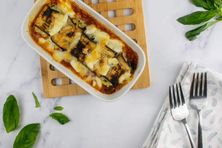 Eggplant rollatini with mozzarella cheese in a casserole dish with fresh basil.