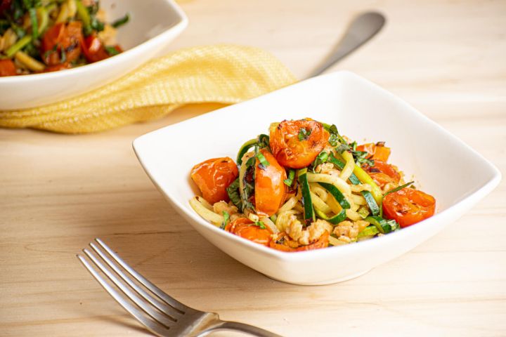 Garlic zucchini noodles with ground sausage and cherry tomatoes in a bowl.