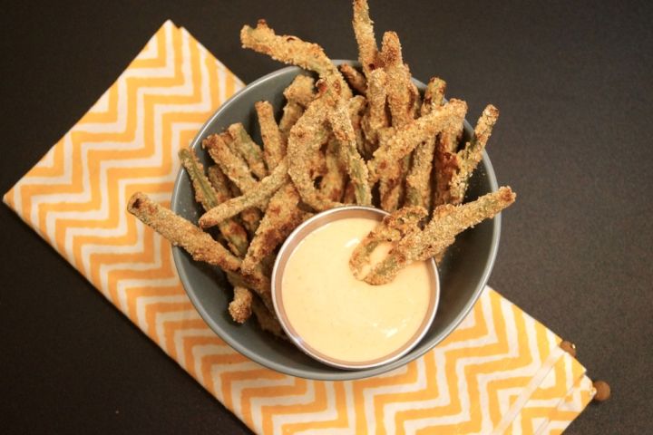Green bean fries in a bowl with a crispy coating and sauce on the side.