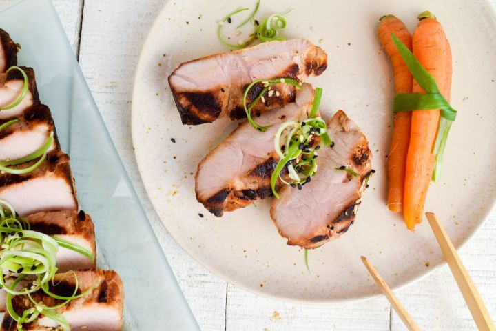 Asian grilled pork tenderloin on a plate with carrots, green onions, and chopsticks.