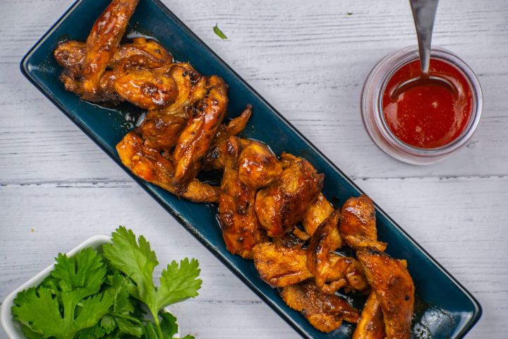 Honey sriracha chicken on a blue plate with Sriracha on the side and lime juice.