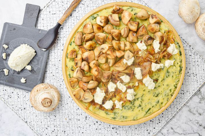 Mushroom spinach polenta with goat cheese on a platter with extra cheese on the side.