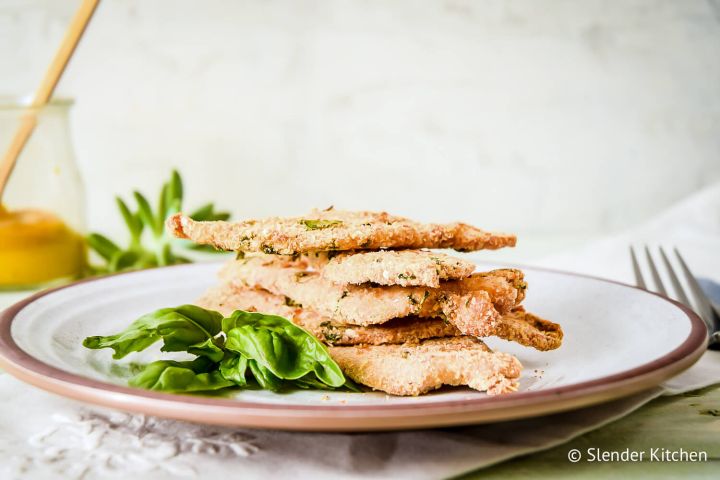 Parmesan crusted chicken piled on a plate with fresh basil and a fork.