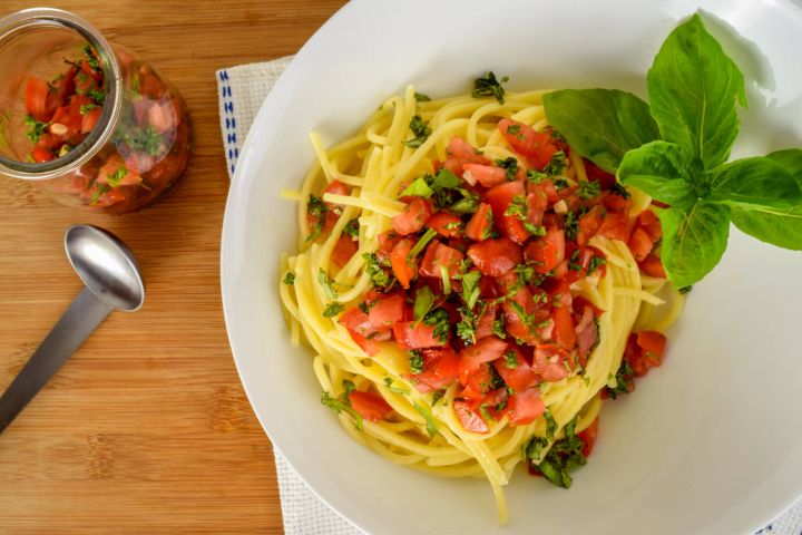 Pasta with fresh tomato sauce and basil on a plate with a blue and white napkin.