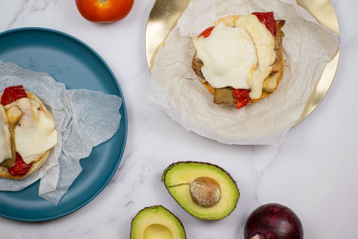 Portobello burger with red peppers, mozzarella, avocado, and red onion on a burger bun.