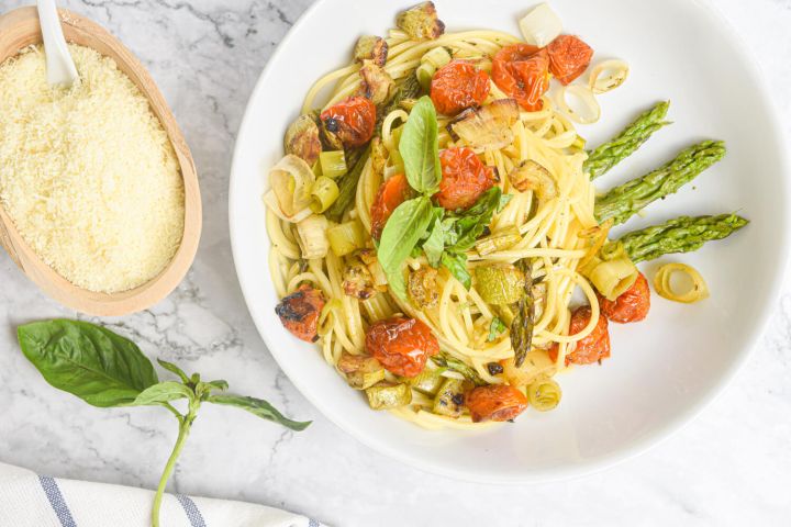 Roasted vegetable pasta with tomatoes, asparagus, onions, and leeks with Parmesan and basil on the side.