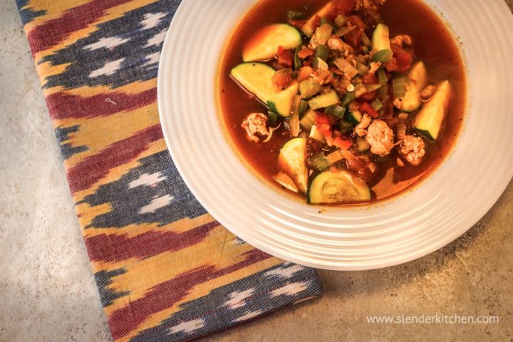 Zucchini sausage soup with tomato broth in a bowl with sliced zucchini, ground sausage, bell peppers, and celery.