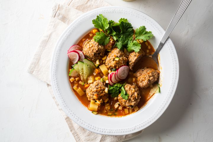 Albondigas soup with Mexican beef meatballs, carrots, zucchini, corn, and onions in tomato broth in a white bowl with cilantro.