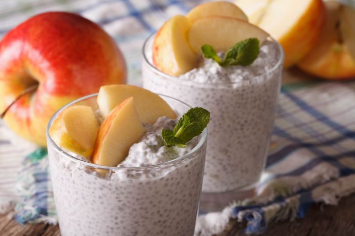 Apple pie chia seed pudding in two glasses with sliced apples and chia seeds.