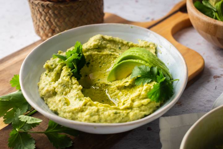 Avocado hummus in a bowl with cilantro and sliced fresh avocado.