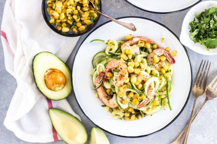 Avcoado zucchini noodles with shrimp and corn served on a plate with lime.