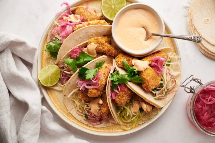 Baja fish tacos with crispy battered fish, cabbage slaw, pickled red onions, and white sauce served in corn tortillas on a plate.