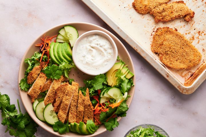 Baked chicken cutlets on a plate with salad and ranch dressing.