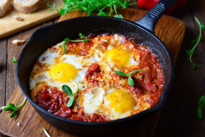 Baked eggs in tomato sauce with parmesan cheese on top in a cast iron skillet.