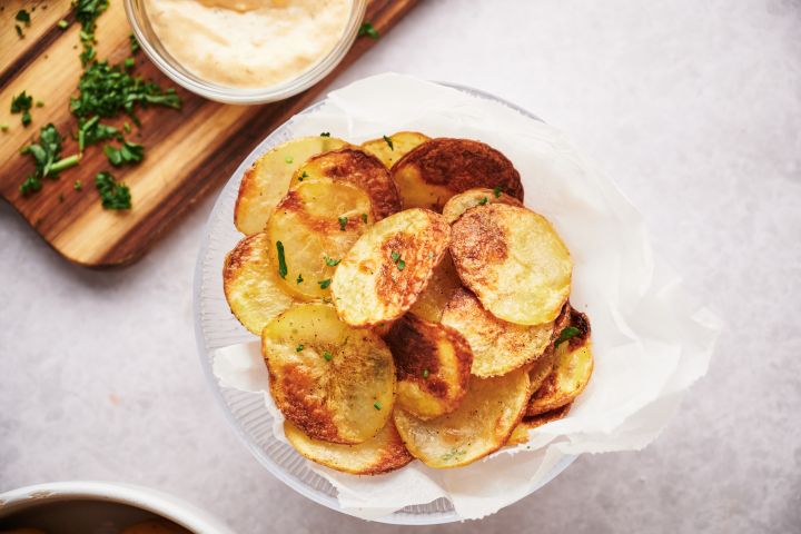 Baked potato chips on parchment paper with with parsley and dipping sauce.