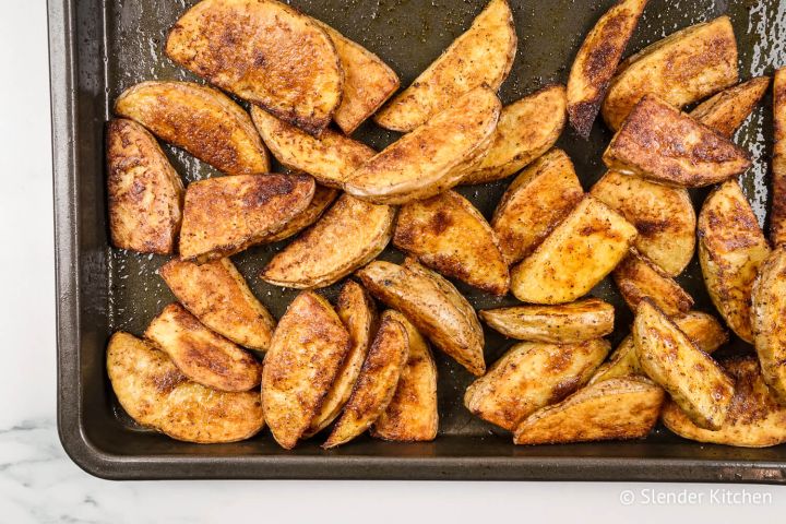 Crispy baked potato wedges on a cooking sheet with paprika, garlic powder, salt, and pepper.