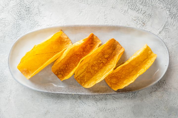 Baked crispy taco shells made with corn tortillas and cooking spray on a white plate.