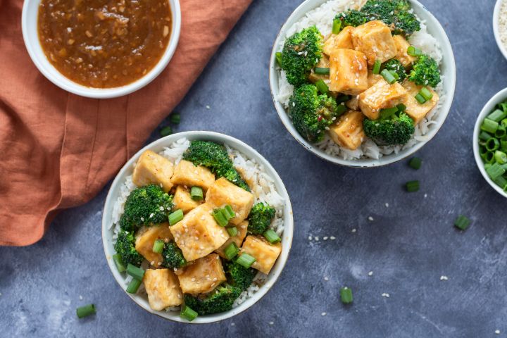 Baked tofu with sweet orange ginger sauce, broccoli, and rice in two bowls.