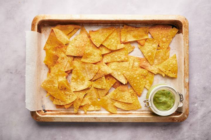 Baked tortilla that are golden browned served on a baking sheet with homemade guacamole.