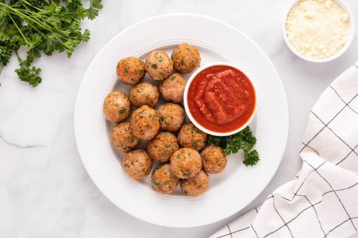 Baked turkey meatballs with parsley and Parmesan cheese on a plate with marinara sauce.