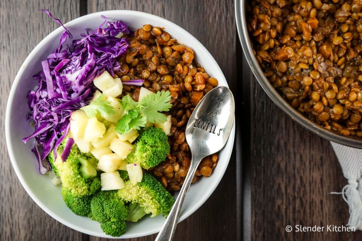 Barbecue lentils in a skillet with a large spoon and colelsaw on the side.