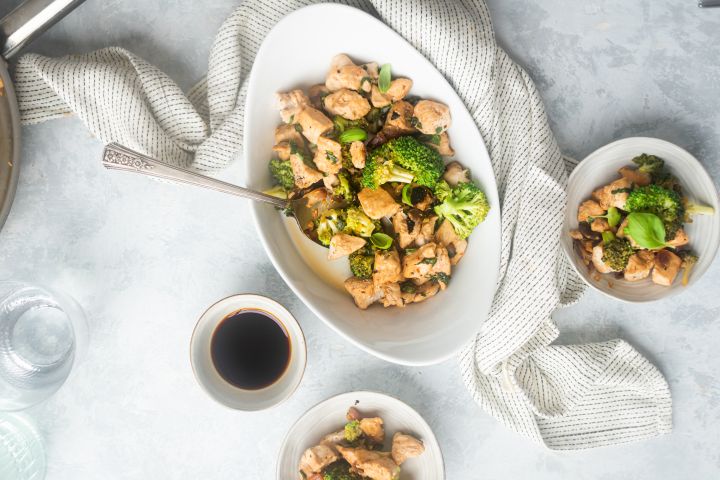 Basil chicken stir fry with broccoli florets, fresh lemon, soy sauce, and red pepper flakes in a bowl with a spoon.