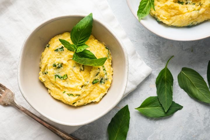 Basil Parmesan polenta in a bowl with fresh basil leaves on top.