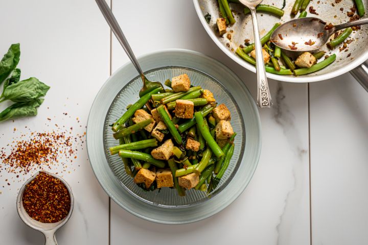Basil tofu with green beans in a glass bowl with a skillet on the side.