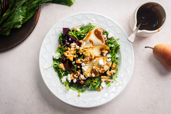 Beet salad with goat cheese, pears, walnuts, arugula, and a blasamic dressing in a white bowll.