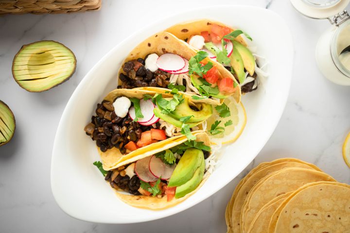 Black bean tacos with chipotle peppers served in corn tortillas topped with avocado, radish, tomatoes, and fresh cilantro.