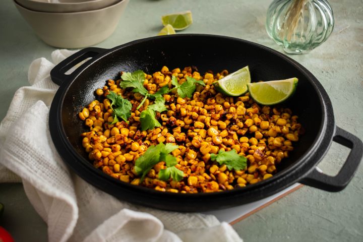 Blackened corn with homemade seasoning served in a skillet with lime wedges and cilantro.