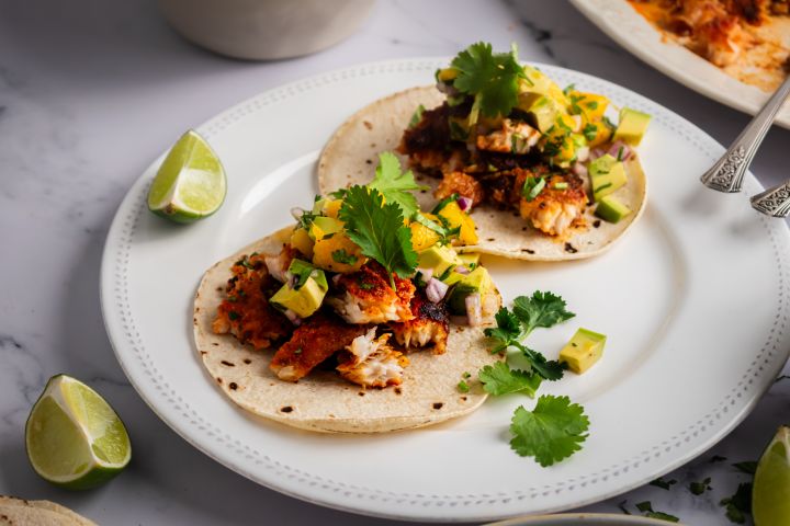 Blackened fish tacos with mango avocado salsa on corn tortillas with fresh cilantro and lime wedges.